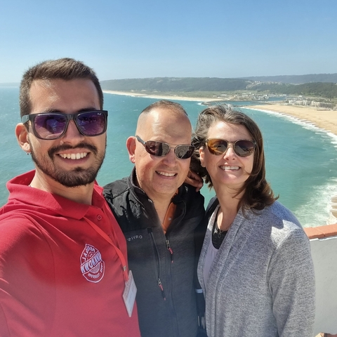 Three people posing for a selfie with a beach in the background.