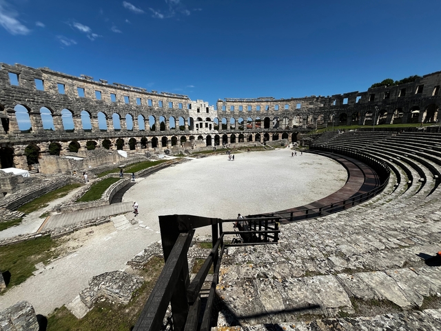       View of a large ancient amphitheater under a clear blue sky.
  