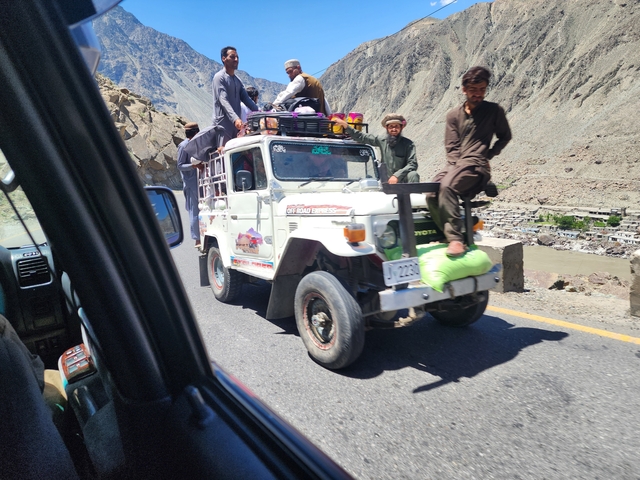       People riding on top of a vehicle on a mountain road.
  