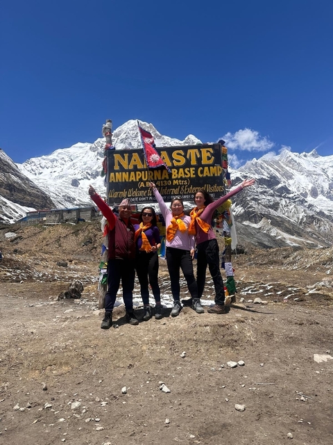       Group of people posing at Annapurna Base Camp with mountains in the background.
  