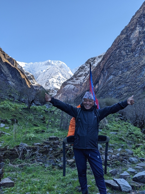       A smiling person giving thumbs up in a mountainous area.
  