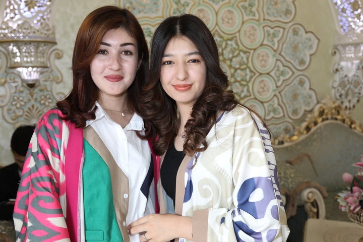 Two women smiling in front of ornately decorated wall.