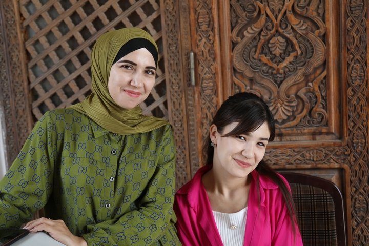 Two women smiling in front of intricately carved wooden panels.