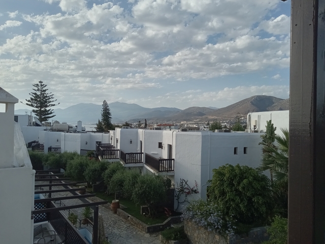       White buildings with mountains and cloudy sky.
  