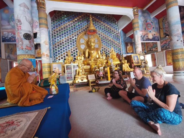       Monk leading a ceremony with people praying in a decorated temple.
  