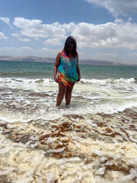 A person standing in shallow water at a rocky beach.