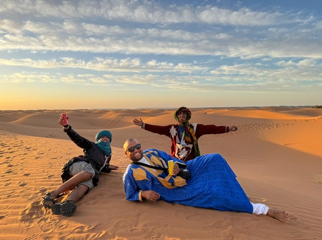 Men wearing traditional attire posing in a desert landscape during sunset.