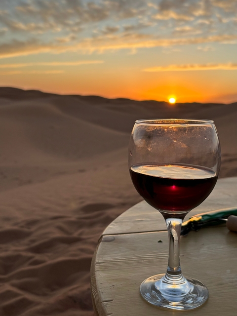 Wine glass with a sunset view over sand dunes.