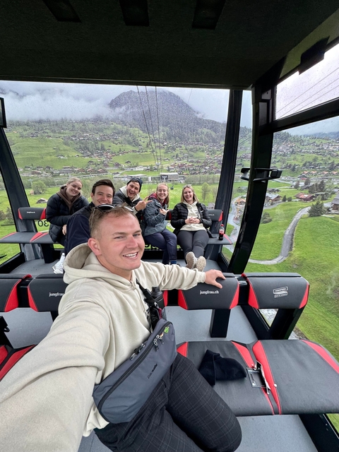 Group taking a selfie inside a cable car with mountains and village in the background.
