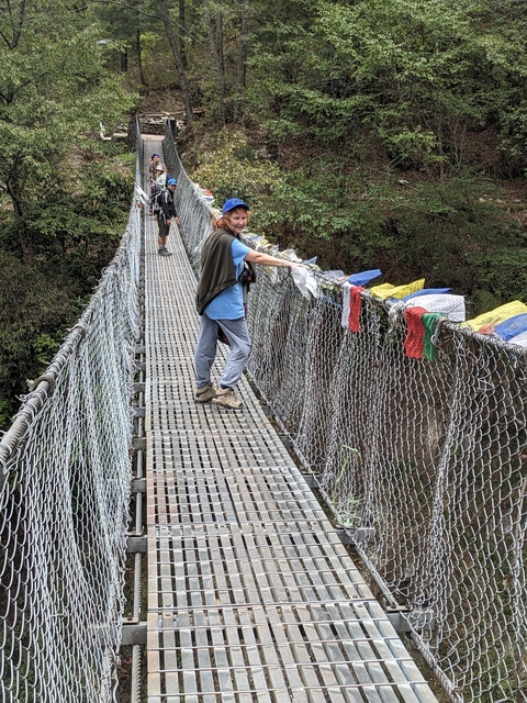       Person crossing a suspension bridge with prayer flags.
  