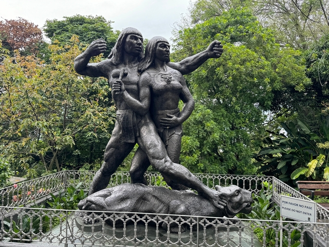       Statue of two figures in a park setting.
  