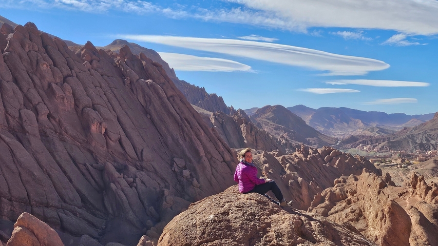 Person sitting on a rock with rugged mountain backdrop.