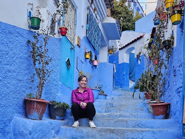 A woman sitting on blue steps in a vibrant alleyway.