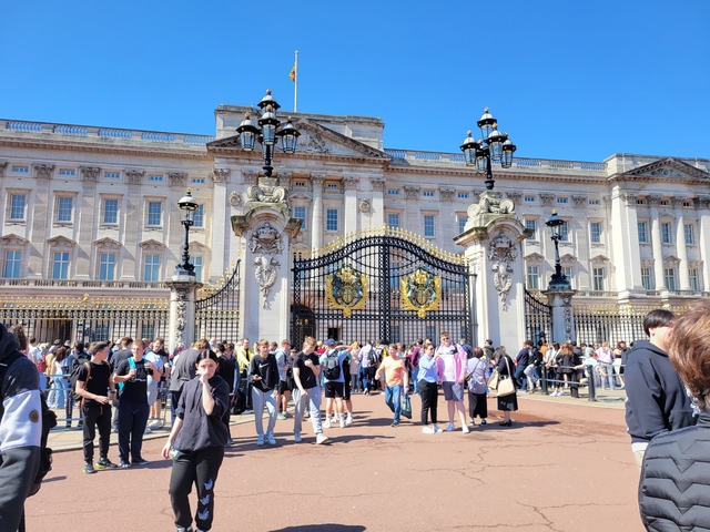 Crowds outside Buckingham Palace with decorative gates.