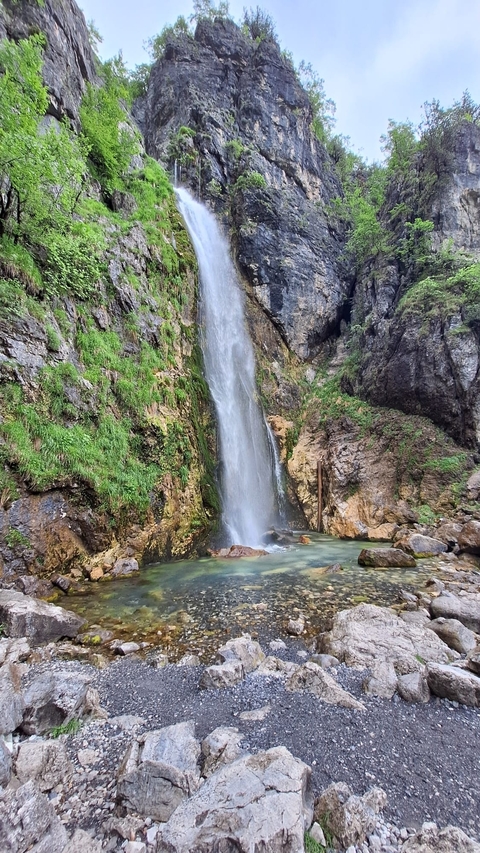A waterfall cascading down a green cliff with rocks and vegetation.
