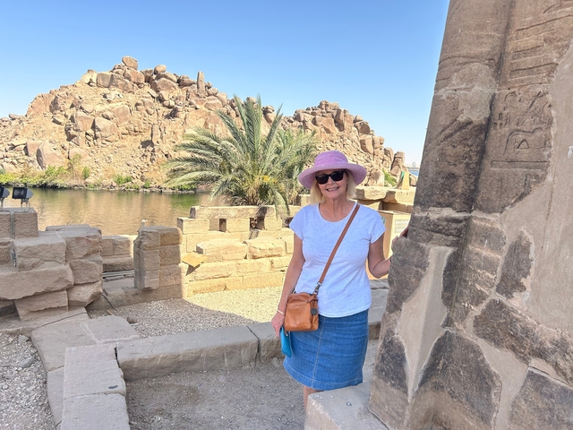 A woman standing near ancient stone ruins with palm trees.