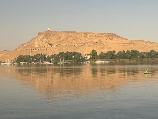 View of riverbank with sailboats under a golden sky.