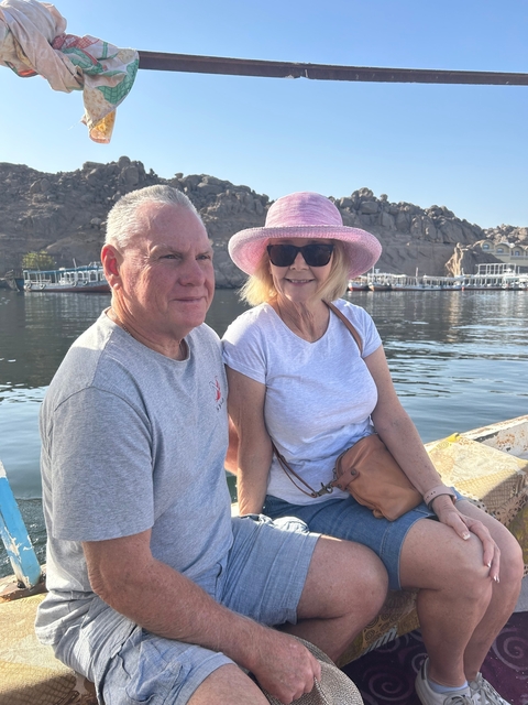 A couple sitting by the water showing boats in the background.