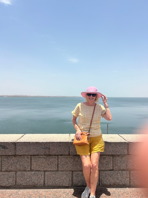       A woman wearing a pink hat standing by a water view.
  