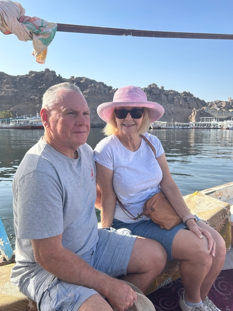 A couple sitting by the water with boats in the background.