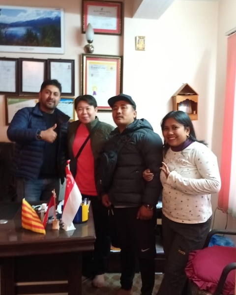 Four people posing indoors with a variety of flags on a table.