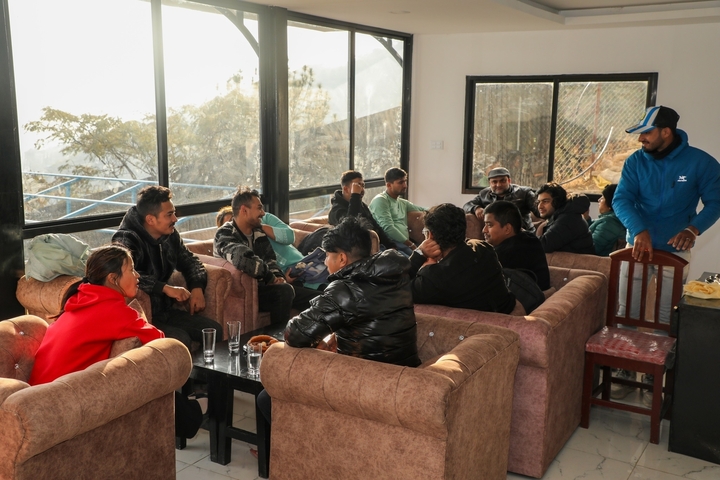 Group of people gathered indoors near large windows.