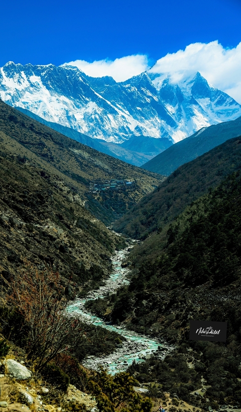 Mountain landscape with a river valley and distant snow-capped peaks.