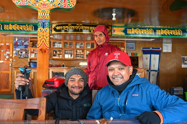 Three men smiling inside a colorful interior with cultural decorations.