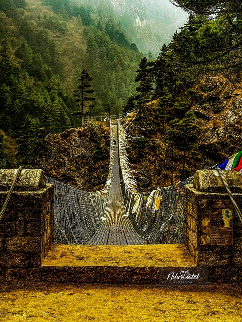      A suspension bridge covered with prayer flags in a mountainous area.
  