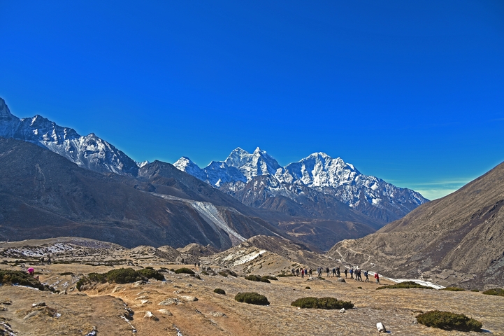       Panoramic view of snow-capped mountains with hikers in the distance.
  
