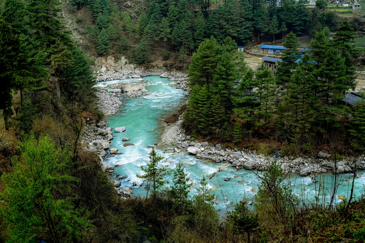 Rushing turquoise river cutting through a forested valley.