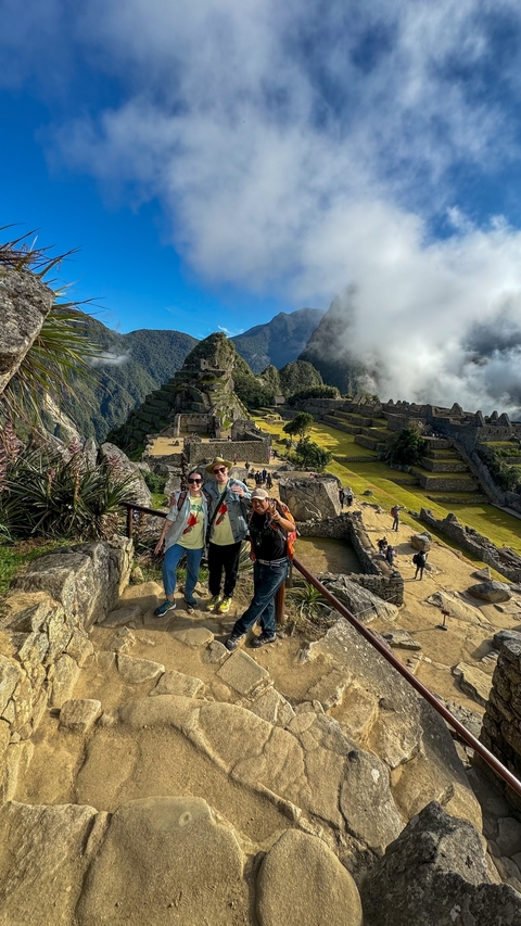       Three people posing at Machu Picchu with ruins and mountains in the background.
  