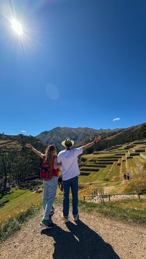      Back view of a couple with arms raised, overlooking Peruvian terraces.
  