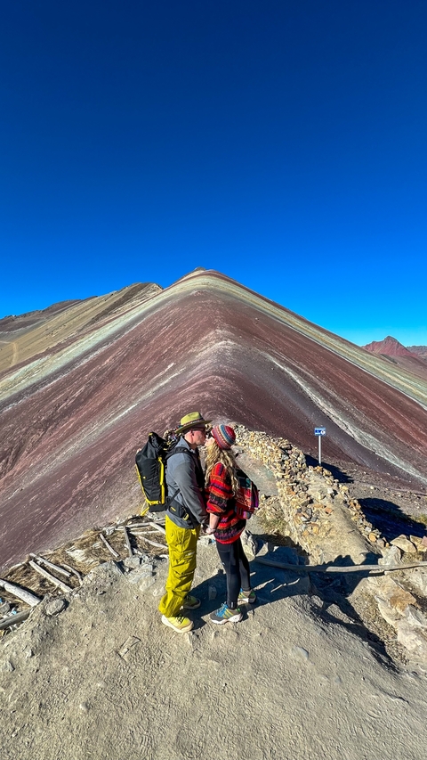       Couple at the colorful Rainbow Mountain with bright blue sky.
  