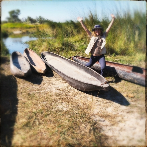 Person standing near traditional canoes by a riverbank.