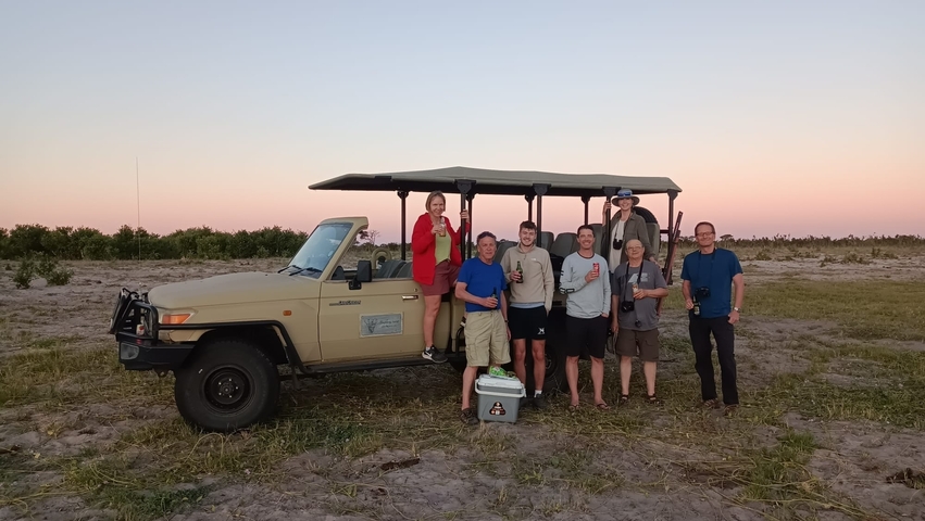 Group posing with a safari vehicle at sunset.