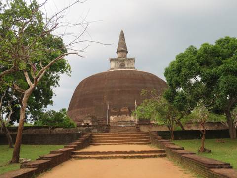 Large ancient stupa with trees and a walkway in front.