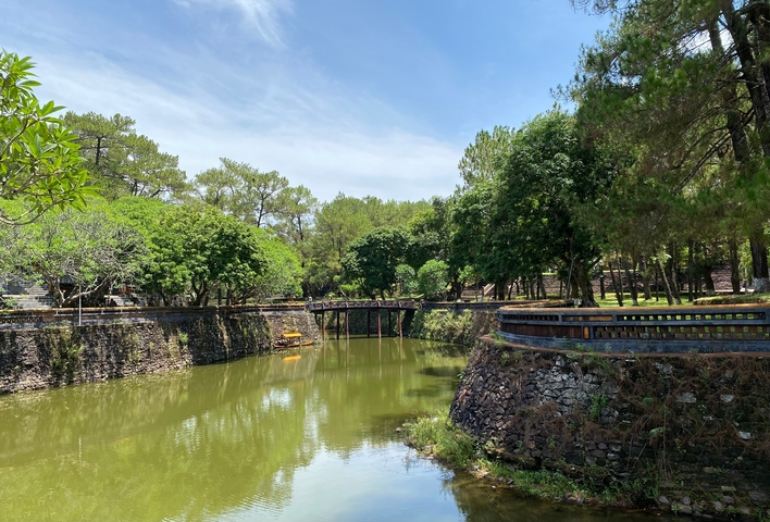       Lush garden with a stone wall and a bridge over water.
  