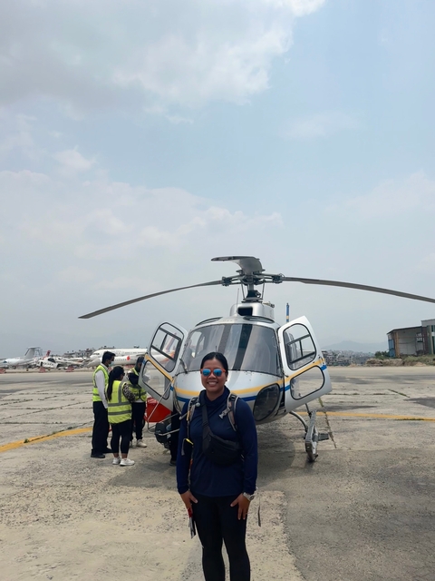 Group standing in front of a helicopter with other aircraft in the background at an airport.