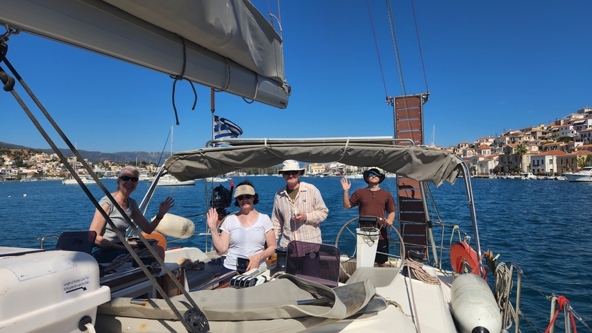       People on a sailing boat with a town in the background.
  