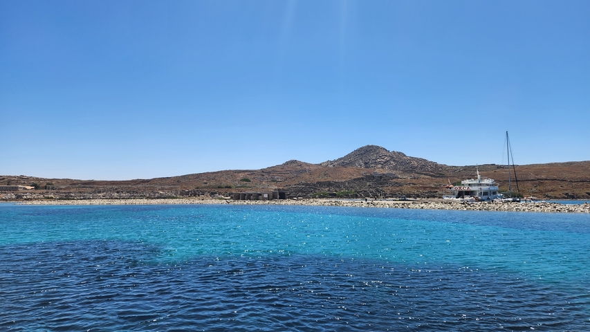       Clear sea with a boat and a mountain in the distance.
  