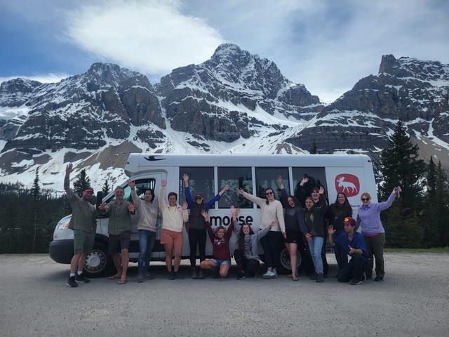Group posing in front of a bus with a mountainous backdrop.