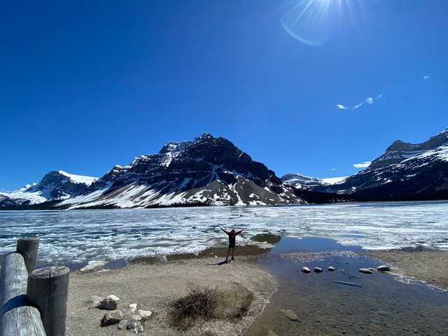 Figure standing triumphant before icy mountain scenery.