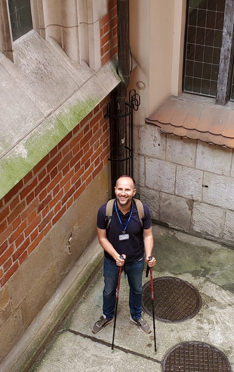       Smiling man standing in a narrow, old stone alleyway.
  