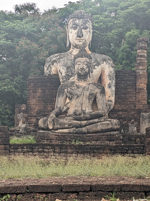       Ancient stone Buddha statue amidst ruins with greenery.
  