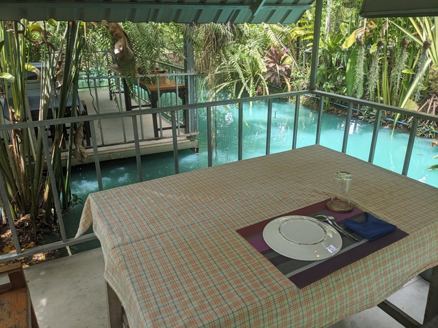       Table set for dining next to a vibrant turquoise canal.
  