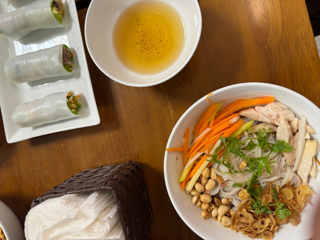 Bowl of Vietnamese noodles with fresh vegetables and spring rolls.