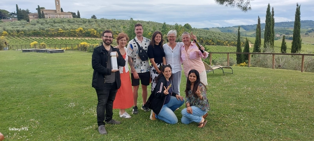 Group of people posing in front of a scenic vineyard.