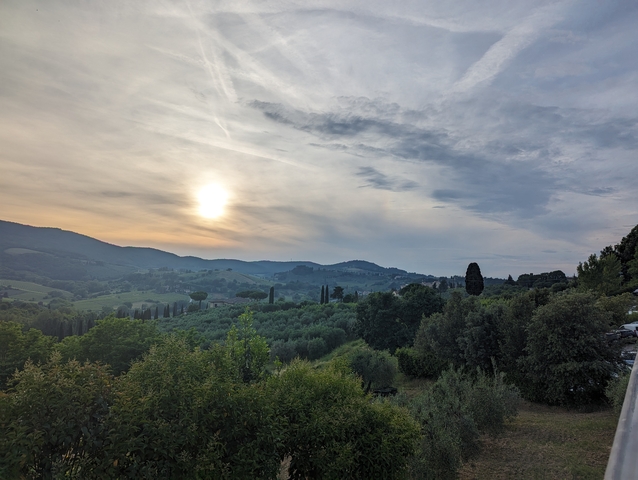Sunset over a hilly landscape with trees and fields.
