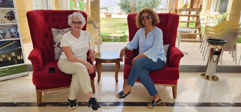 Two women sitting on red armchairs in a hotel lobby.
